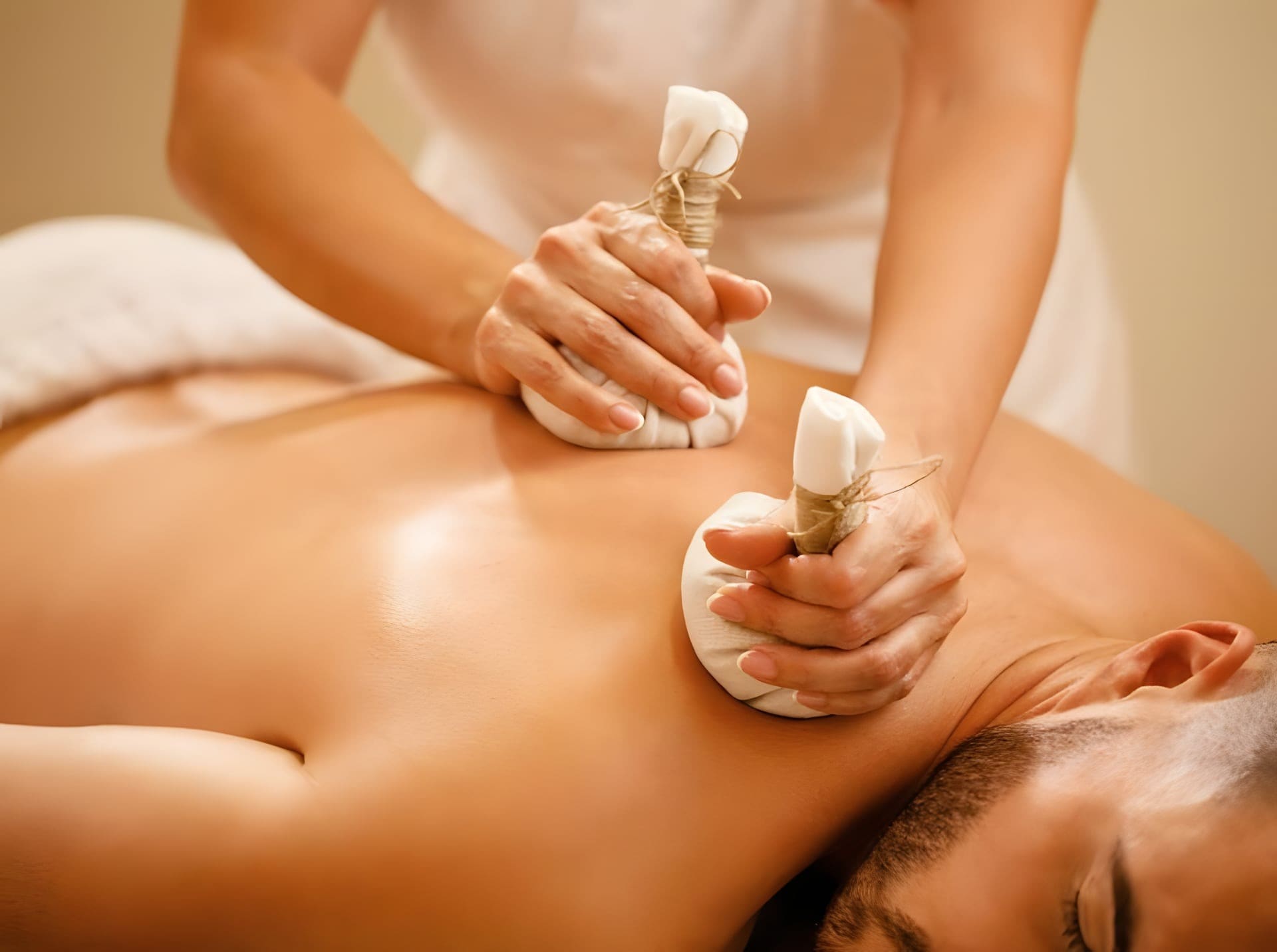 Twee handen masseren een rug met warme kruidenstempels